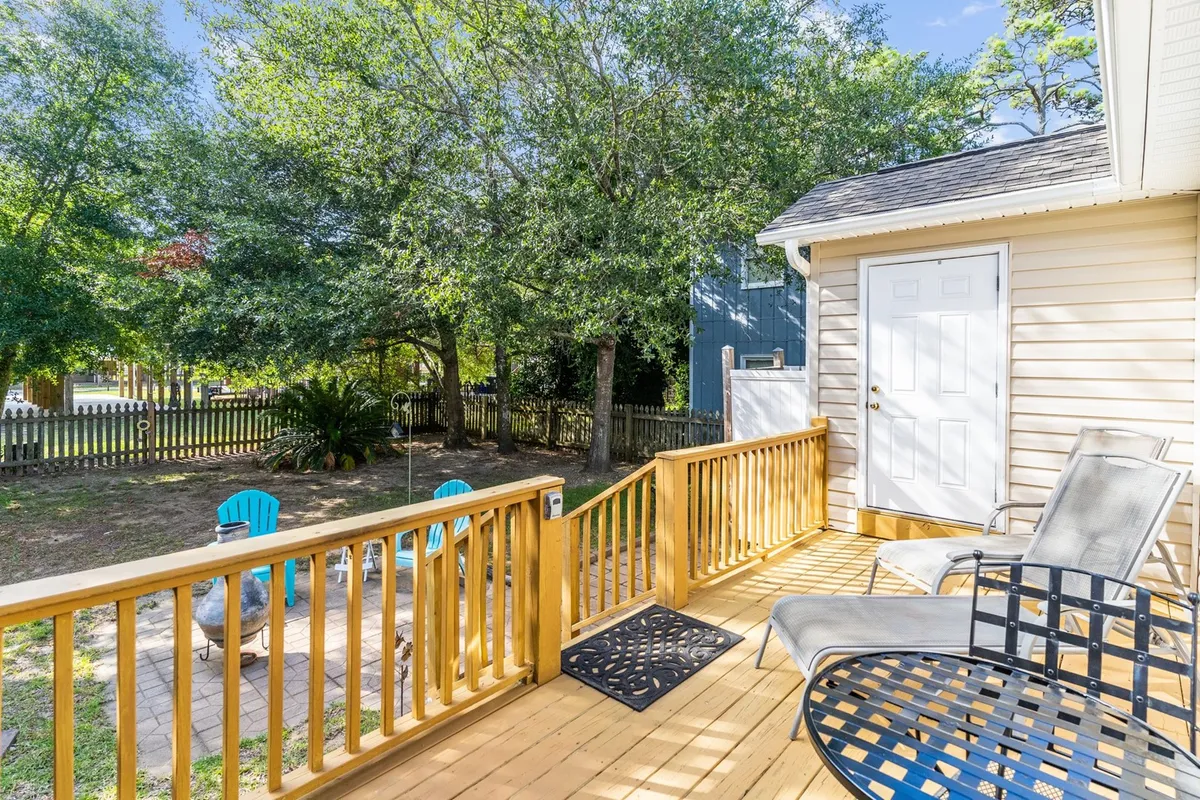 This image shows a wooden deck outfitted with blue Adirondack chairs, a doorway leading inside, and abundant surrounding greenery. The setting suggests a relaxed, social outdoor environment ideal for enjoying fresh air, connecting with friends, and taking in the natural beauty right at home.