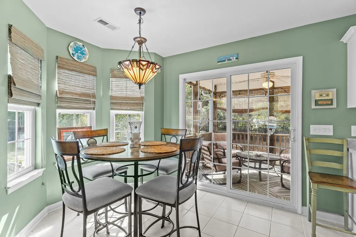 A warm dining area with a round dining table set for four, a striking chandelier above, and large glass doors that invite in natural sunlight and offer a view to the outside. The setup encourages casual dining and togetherness, with a seamless connection between indoor and outdoor spaces.