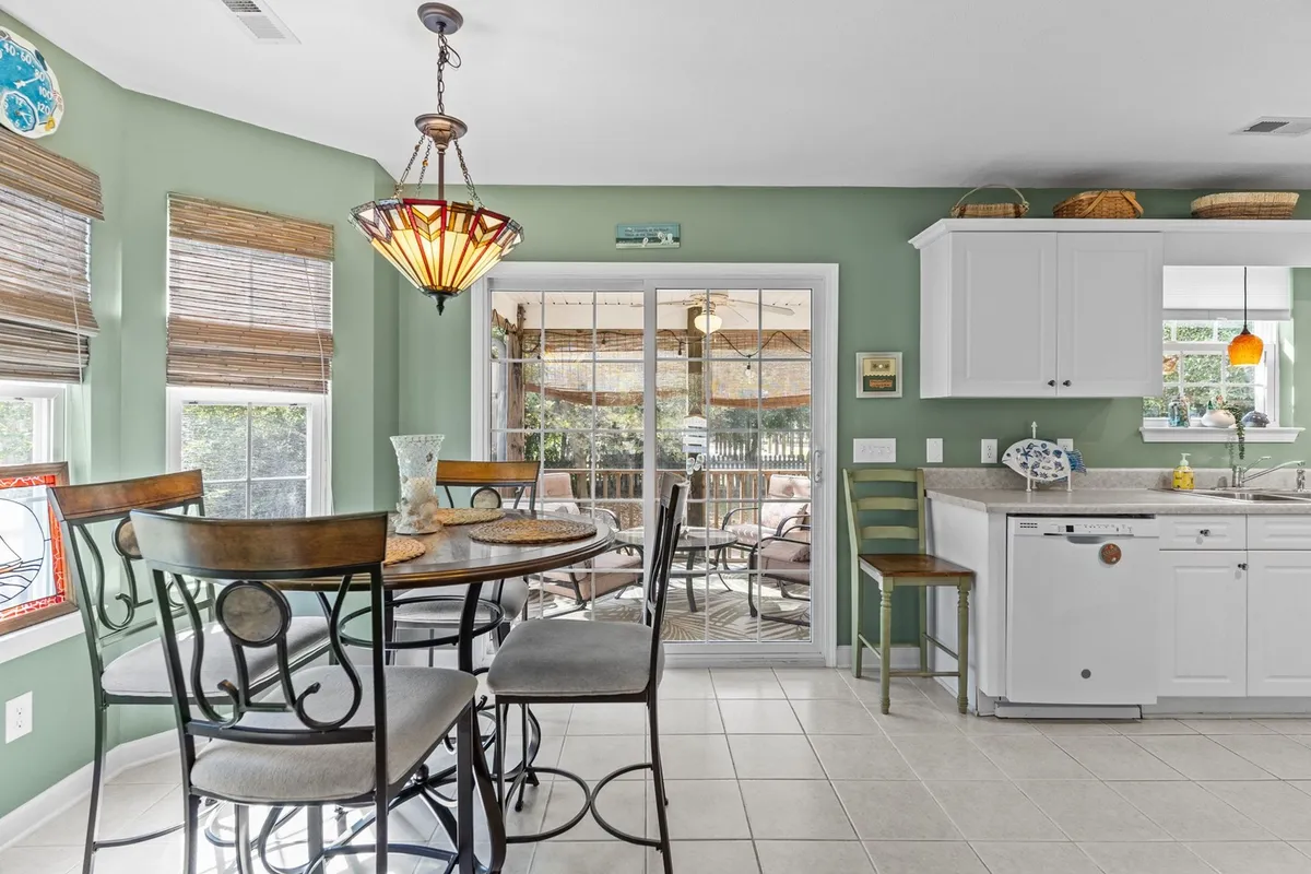 A bright dining area featuring a round table, stylish light fixture, and sliding glass door that connects the indoors with the outdoors. Kitchen cabinetry is visible, emphasizing open, accessible spaces for gathering, dining, or savoring morning coffee.