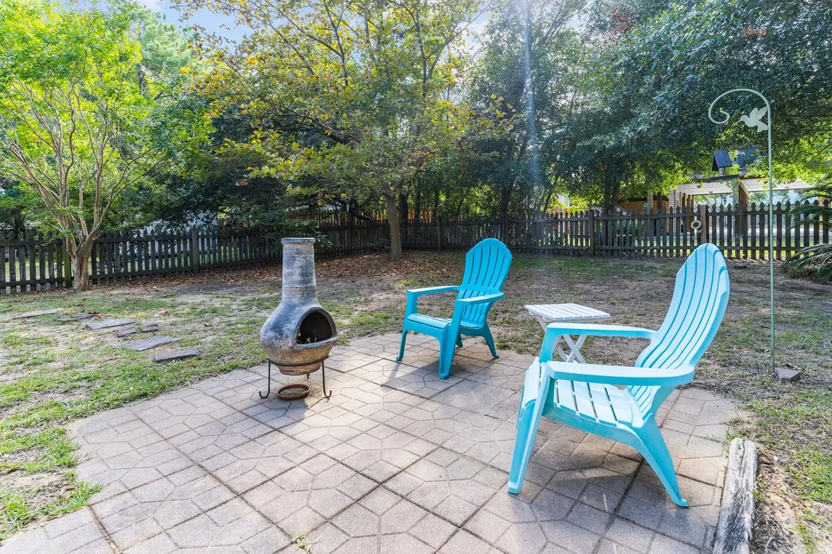 An outdoor patio adorned with blue Adirondack chairs and a chiminea, surrounded by patio stones and lush greenery. The scene is set for relaxed outdoor gatherings, sipping drinks under the stars, and enjoying the tranquility of nature with friends or family.