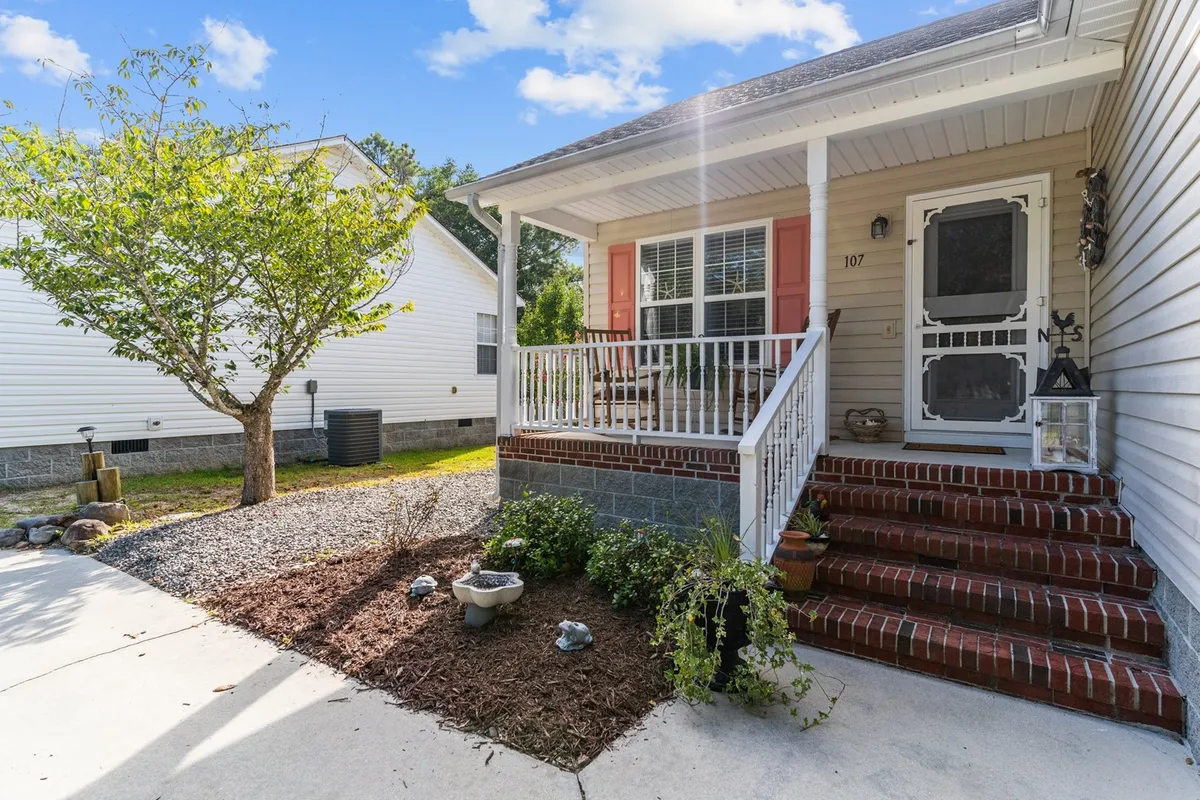 This exterior image features a cheerful front porch with brick steps, a landscaped garden, and decorative stones. The porch is set up for socializing, watching sunsets, and enjoying time with neighbors or family, making it a focal point for both relaxation and community connection.
