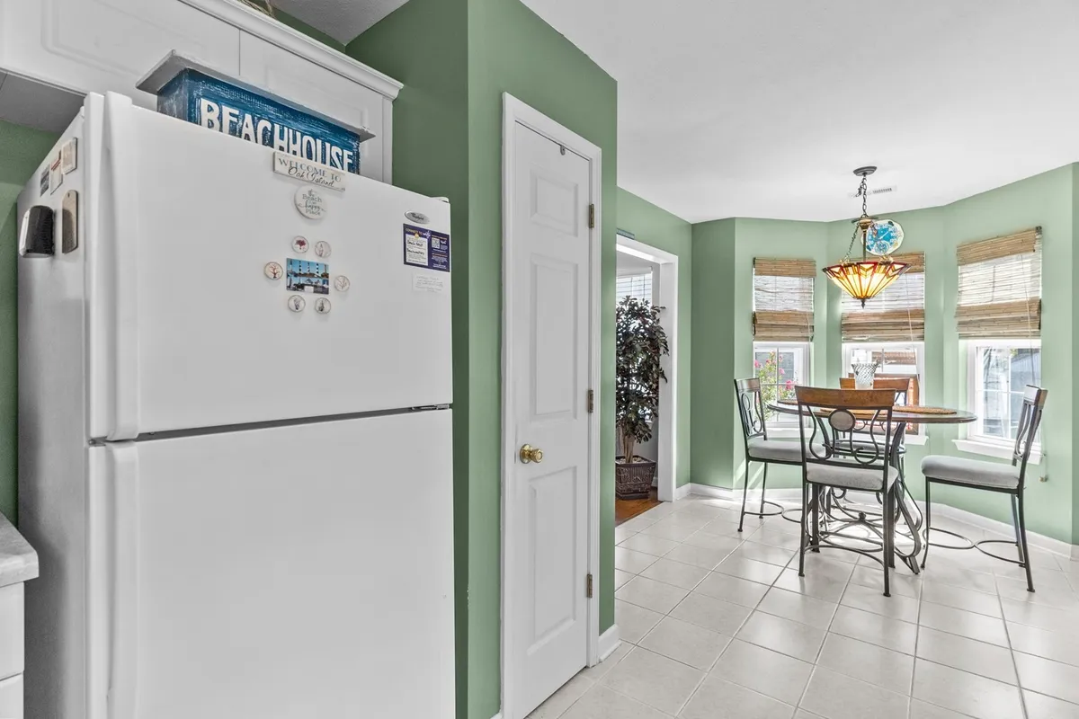 A kitchen-focused scene with a full-size refrigerator, dining table, windows for natural light, and a chandelier that creates a cozy dining atmosphere. The setup highlights meal preparation and casual dining.
