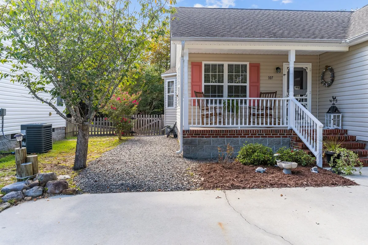 A detailed exterior image showing the front porch adorned with decorative elements and inviting landscaping. The scene captures relaxation, gardening, and small social gatherings, embodying the casual charm of Oak Island living.