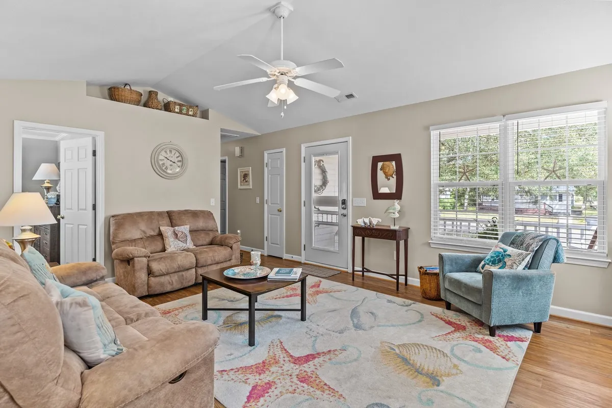 A cozy living room furnished with comfortable sofas and a coffee table, accented by a decorative rug. The space invites natural light through windows, creating a welcoming atmosphere perfect for relaxing with a book or enjoying a cup of coffee.