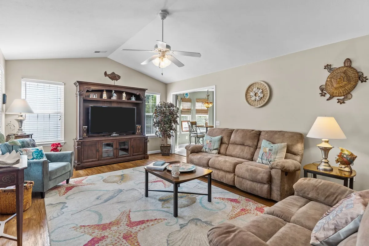 A cozy living room featuring a comfortable plush sofa, coffee table, colorful area rug, decorative wall art, and a television unit. The space exudes a relaxed and welcoming atmosphere, ideal for lounging, watching family movies, or gathering for intimate conversations.