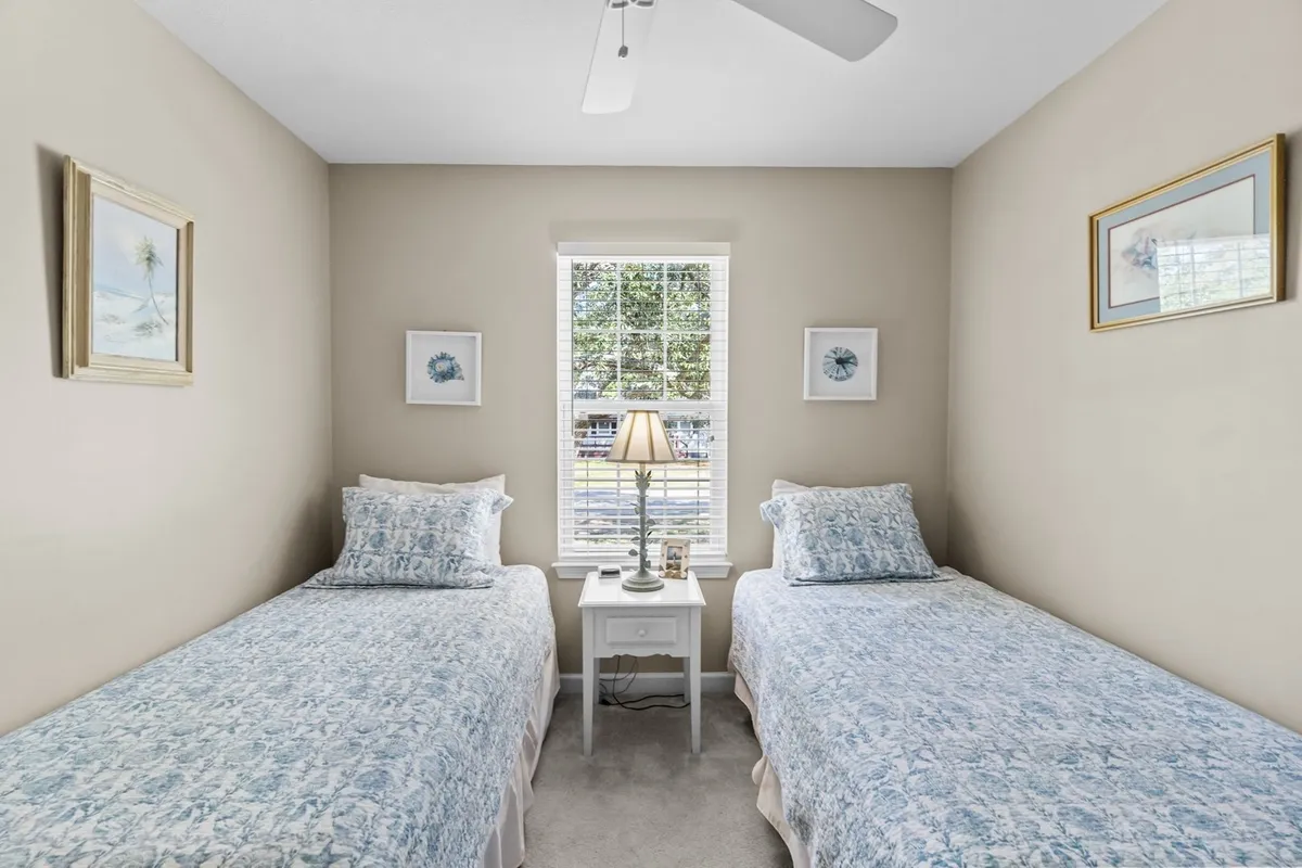A bedroom with two twin beds, a table lamp, and a window letting in natural light. The arrangement encourages quiet mornings, reading, and late-night chats, all in a relaxed, uncluttered setting.