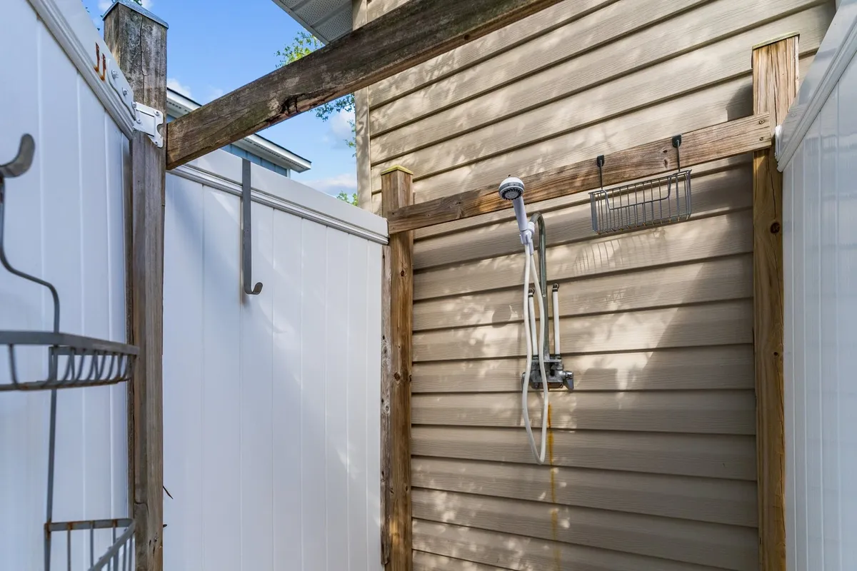 An outdoor shower nestled against a wooden structure with white fencing provides a refreshing post-beach rinse solution. The fencing also subtly reinforces the pet-friendly, enclosed aspect of the yard.